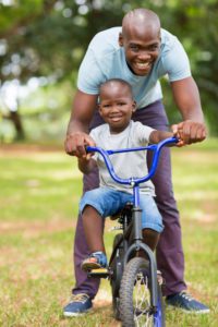 loving african father helping son ride a bike outdoors